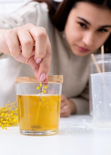 Woman making decorative aroma candle at table with mimosa closeup