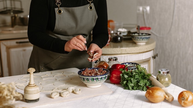 Woman making dumplings at kitchen with ingredients