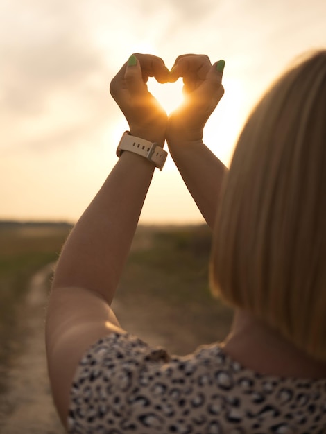 Woman making heart symbol with her hands at sunset outdoors