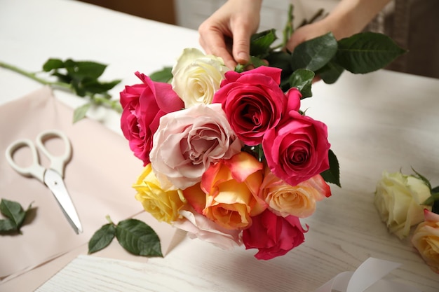 Woman making luxury bouquet of fresh roses at white wooden table closeup