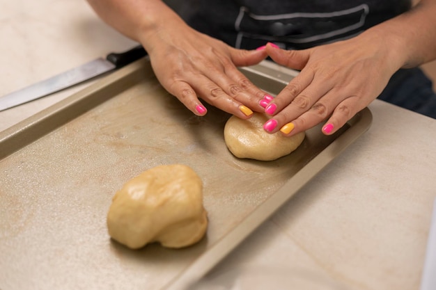 Woman making pan de muerto at home arranging the dough on a baking sheet