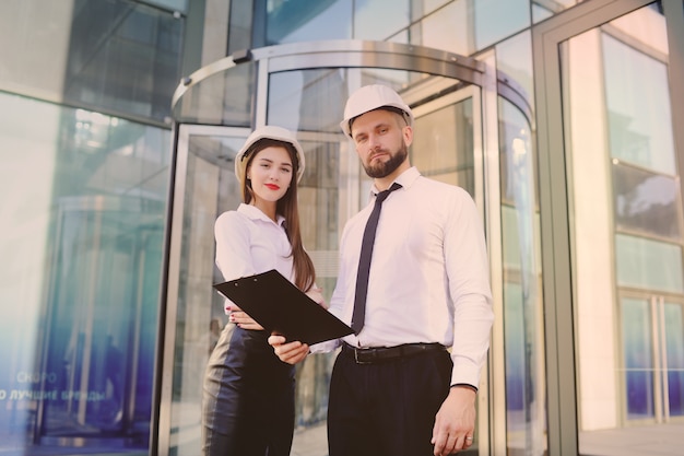 A woman and a man in business clothes and in white construction helmets discuss a construction plan or a contract signature