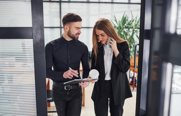 Woman and man in formal clothes with documents talking to each other in the office.