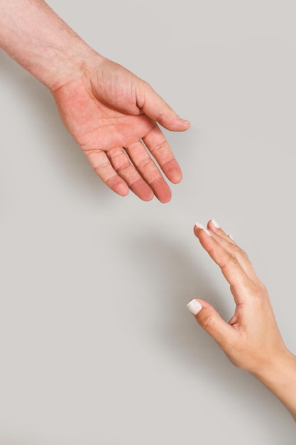 Woman and man hands triying to hold each other on a gray background with copy space