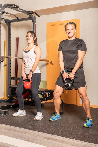 Woman and man looking at camera doing kettlebell swing exercise at gym. Concept of exercises with equipment in gym.