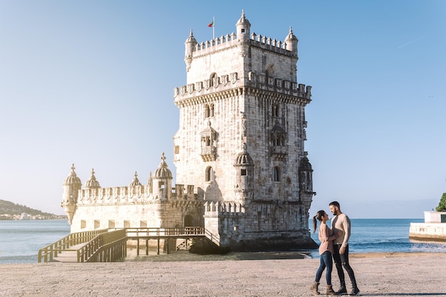 Woman and man looking at each other with the belem tower and the Tagus river in the background in Lisbon Portugal