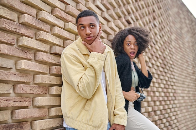 Woman and man posing at camera near brick wall