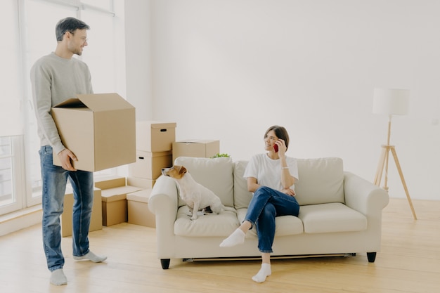 Woman and man real estate renters pose in empty living room, female sits on couch in middle of room