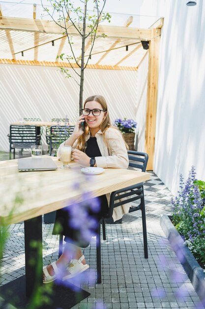 Photo a woman manager sits on an outdoor terrace in a cafe and works online with coffee female freelancer works remotely online while sitting in a summer cafe remote work