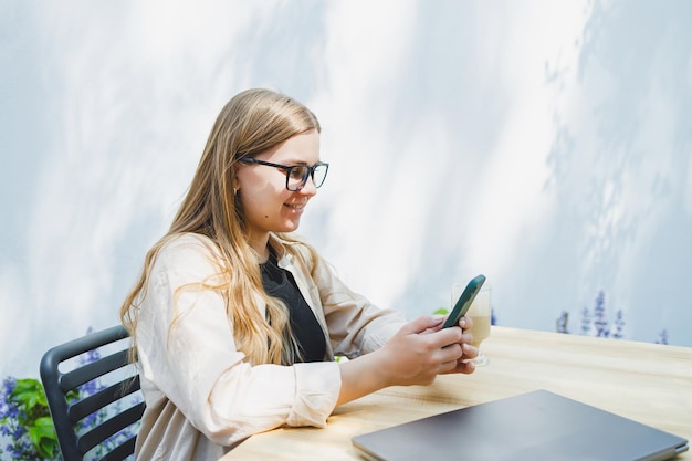 A woman manager sits on an outdoor terrace in a cafe and works online with coffee Female freelancer works remotely online while sitting in a summer cafe Remote work