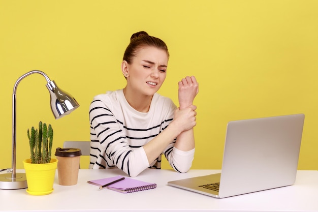 Woman manager sitting at workplace with laptop and holding sore wrist suffering pain in injured hand