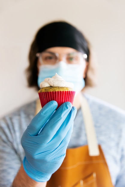 Woman in mask and gloves holding cupcake