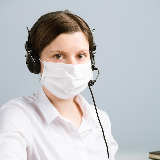 Woman in the mask with a headset, using computer and notebook. Call center operator working in the pandemic.