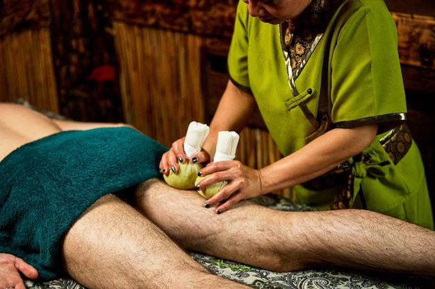 Woman massages patient leg with herbal bags in spa salon