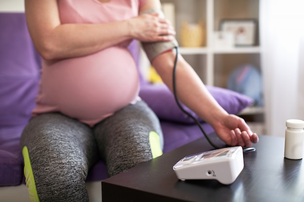 A woman measures blood pressure with an electronic pressure gauge, headache during pregnancy, poor health. selective focus on medical equipment