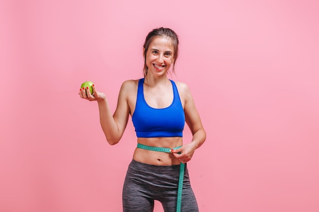 woman measures waist and shows green Apple on pink wall