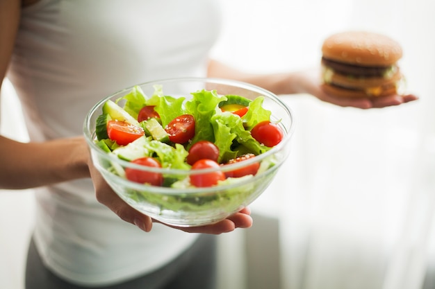 Woman Measuring Body Weight On Weighing Scale Holding Burger and Salat.