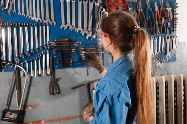 Woman mechanic stands in the garage near the stand with the keys and makes a choice