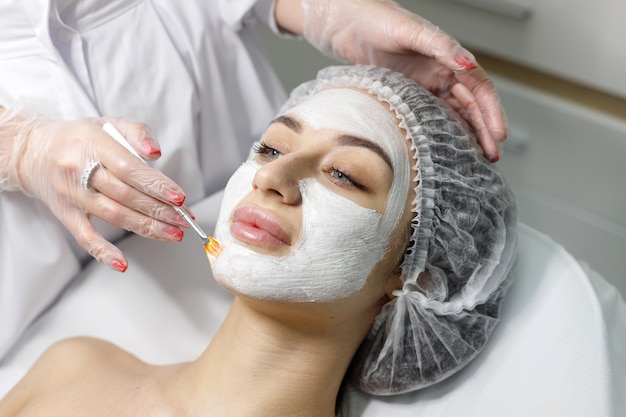 Woman in medical cap makes mask on face of beautician