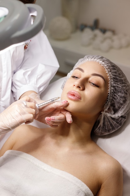 Woman in medical cap makes a shot in the lips of a beautician