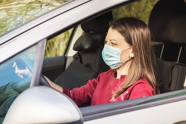 Woman in medical mask driving a car. lady keeping social distance.