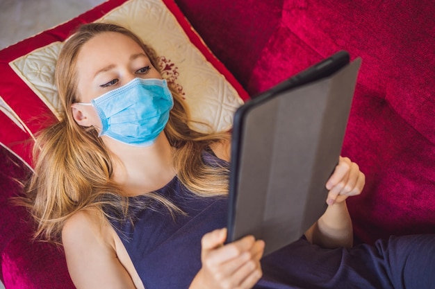 Woman in medical mask reads a book on the couch Home quarantine Stay at home Coronovirus