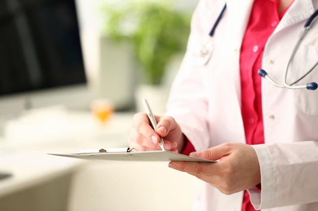 Woman medicine doctor with silver pen writes on a clipboard closeup