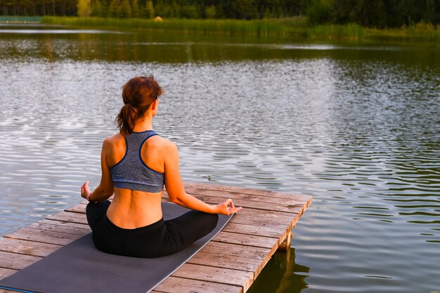 A woman meditates in nature by the lake. The concept of realizing the meaning of life.