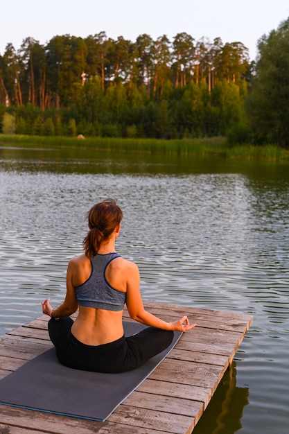 A woman meditates in nature by the lake. The concept of realizing the meaning of life.