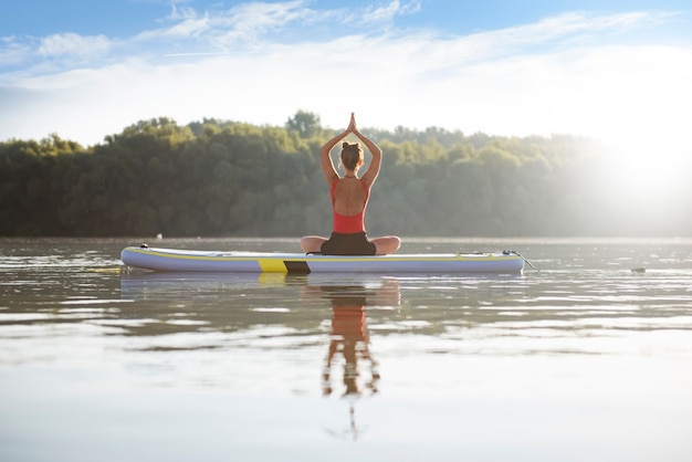 Photo woman meditating during sunrise in paddle board