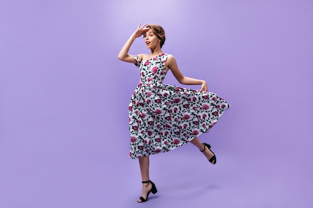 Woman in midi dress looks into distance on purple background Fashionable young lady in colorful clothes jumping on isolated backdrop