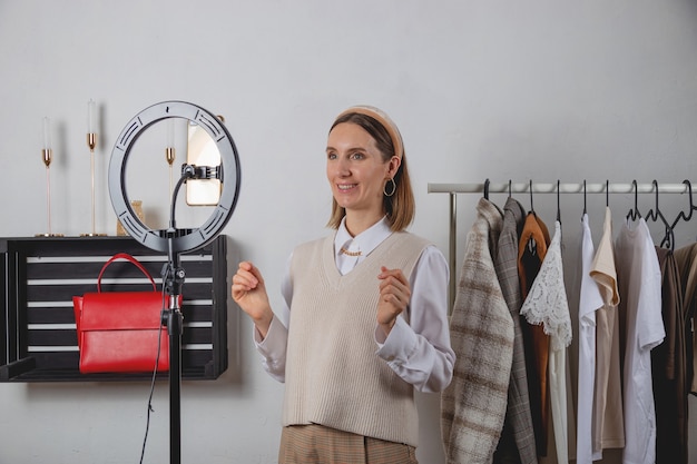 Woman millennial fashion stylist records fashion video on smartphone with ring lamp