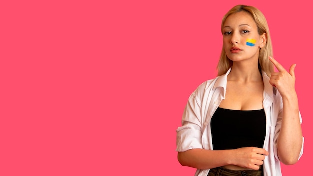 Woman of model appearance with the flag of Ukraine on her face holds posing on a pink background