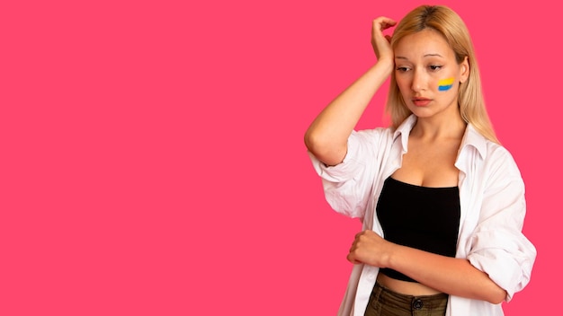 Woman of model appearance with the flag of Ukraine on her face holds posing on a pink background