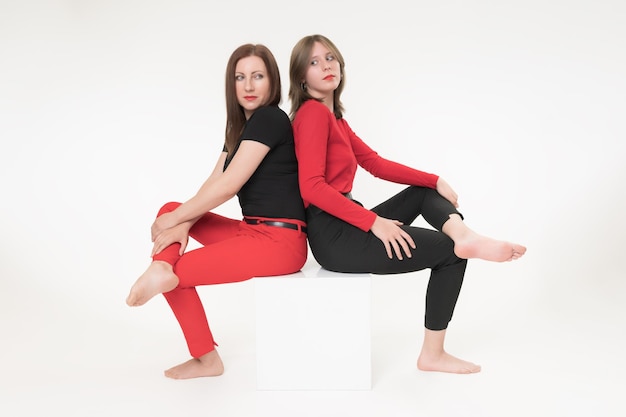 Woman mom and daughter sitting with their backs to each other on cube on white background