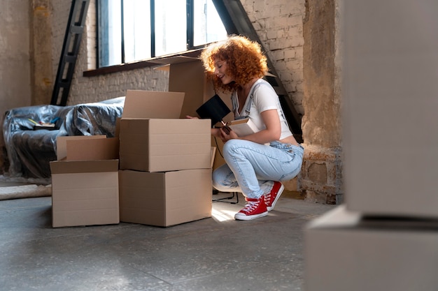 Woman moving in to new home and sorting cardboard boxes with belongings