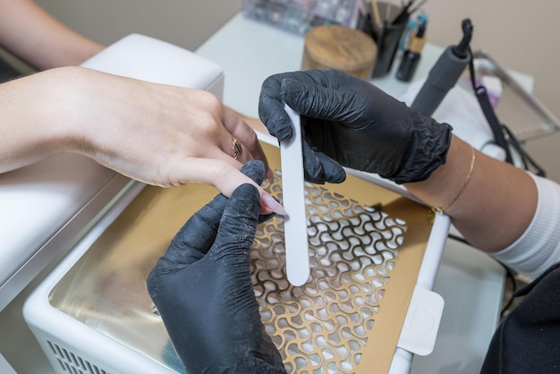 A woman in a nail salon gets a manicure in a beauty salon from a beautician who uses a nail file Nail care concept Modeling of nails Closeup of filing nails with a nail file