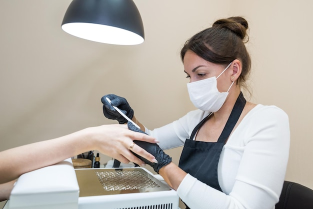 A woman in a nail salon gets a manicure in a beauty salon from a beautician who uses a nail file Nail care concept Modeling of nails File your nails with a nail file