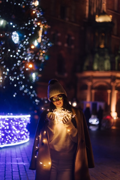 Woman near a Christmas tree on the street with garlands in her hands