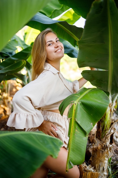 Woman near green leaves of banana bushes on nature in a park in a tropical place, she is in a beige skirt and a blouse