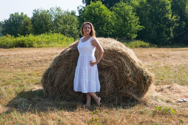 A woman near a haystack in a white dress Morning sunrise in nature in the field