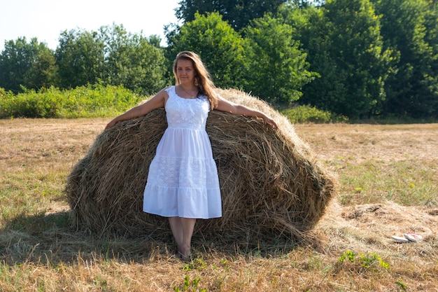 A woman near a haystack in a white dress Morning sunrise in nature in the field