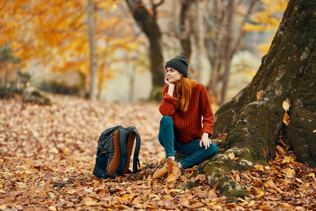 Photo woman near tree and backpack for travel fallen leaves autumn forest high quality photo