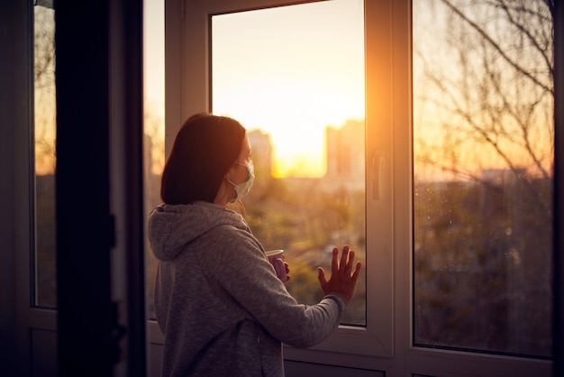 Woman near window at sunset in isolation at home for virus outbreak. Stay home concept