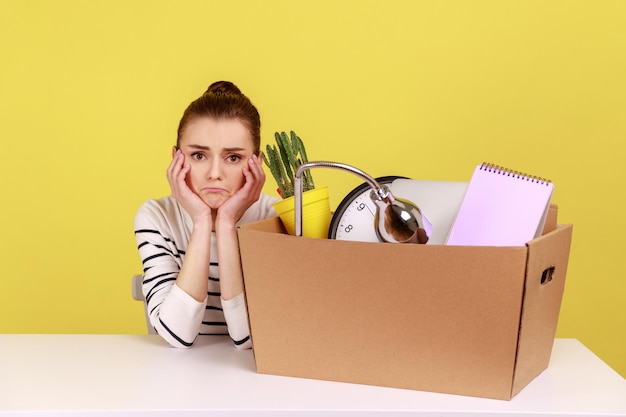 Woman office worker sitting at workplace with cardboard box with her things dismissal bankruptcy