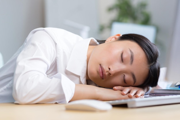 Woman office worker tired asian sleeps on the desk overtired sleeps in the day