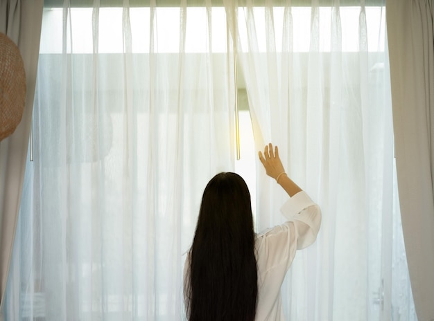 A woman opens a curtain in the morning sunlight relaxing and holiday concept