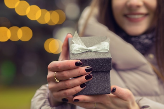 Woman opens a small gift box with a bow at the street with bokeh light