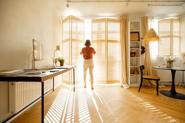 Woman opens window blinds at sunny room