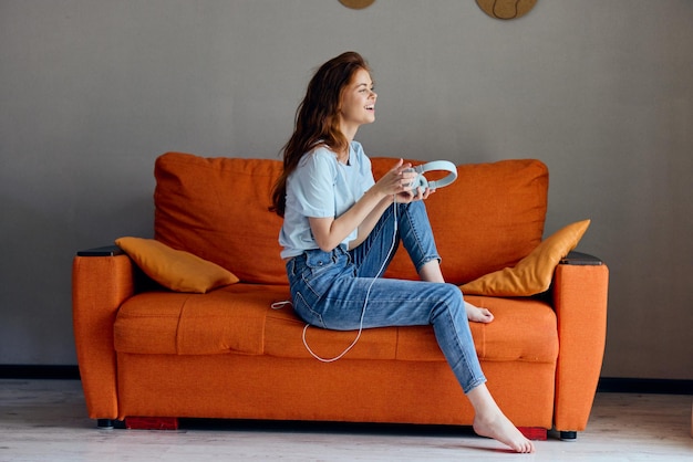 Woman on the orange sofa listening to music with headphones Lifestyle